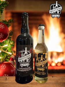 Zwei winterliche Sorten, Honig-Met und Langensalzaer Kaminfeuer, der Dreitürme Brauerei Bad Langensalza stehen auf einem Tisch vor einem Kaminfeuer. An der Seite sieht man die Nadeln eines Weihnachtsbaumes.